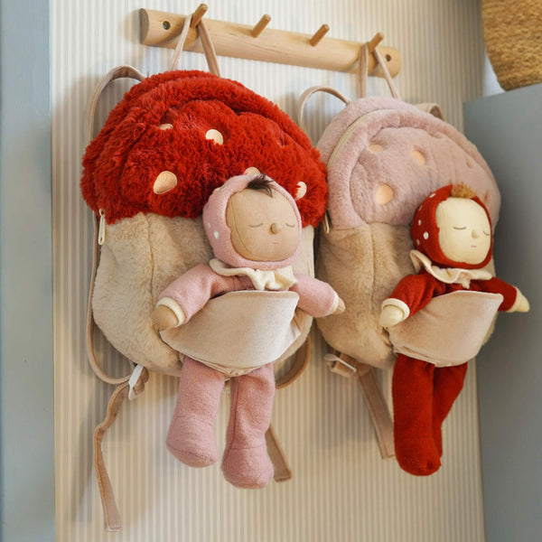 Two plush dolls with red and pink outfits hanging on a hook against a neutral background.
