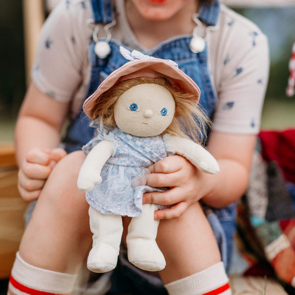 Child holding a doll with a blue dress and pink hat