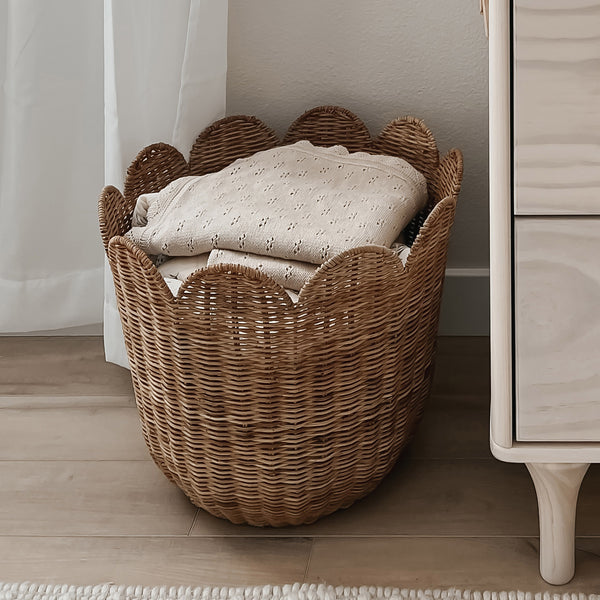 Functional brown rattan storage basket. Featuring scalloped edges, this basket is the perfect size for storing toys, laundry, towels and more. Use as décor storage in nurseries, bedrooms or anywhere in your home.