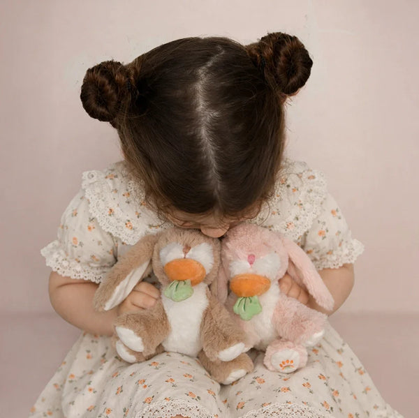 Child holding two plush bunnies against a pink background