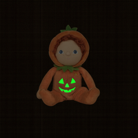 Plush toy in a pumpkin costume with glowing green face on a black background
