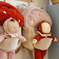 Two plush dolls with red and pink outfits hanging on a hook against a neutral background.