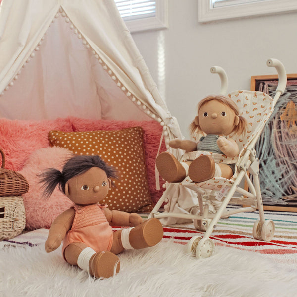 Two dolls in a child's room with a teepee and colorful pillows.