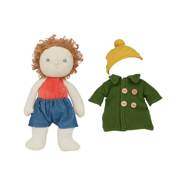 Stuffed doll with red shirt, blue shorts, and yellow hat next to a green coat on a white background