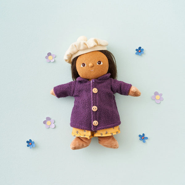 Toy figure wearing a purple coat and yellow dress on a light blue background with flowers.